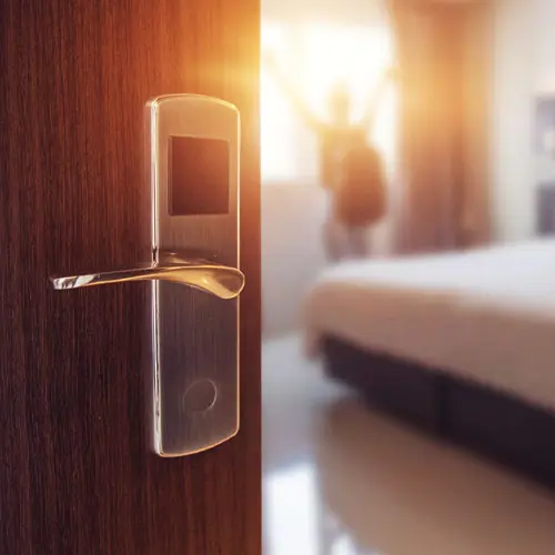 A hotel room door handle with a woman standing in front of it.