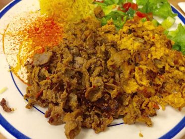A plate with meat, rice and salad on it.