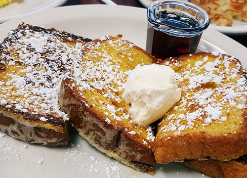 A plate of french toast with powdered sugar and syrup.