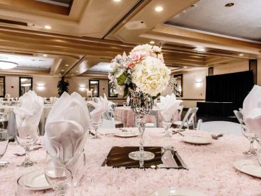 A large ballroom with white tablecloths and pink centerpieces.