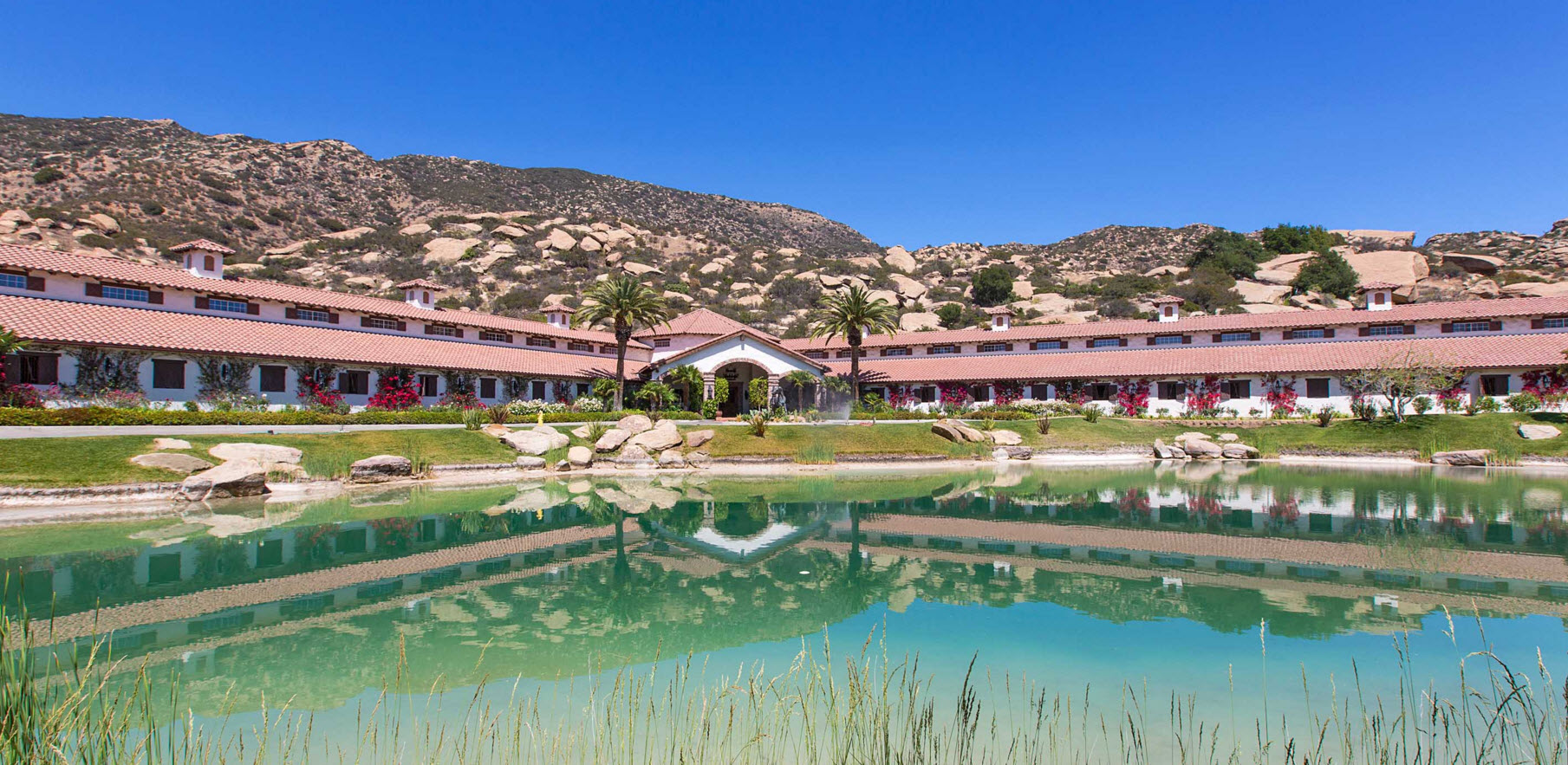A hotel with a pond and mountains in the background.